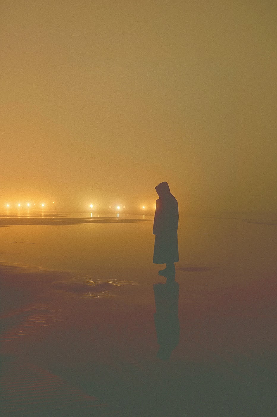 A lone hooded person on a foggy beach at the seaside, sunken in nostalgia, lights shining in the far distance. An ethereal, minimalist new media AI artwork on the beauty and magic of solitude, inspired by the cinematic look of Blade Runner 2049. | Wall Art