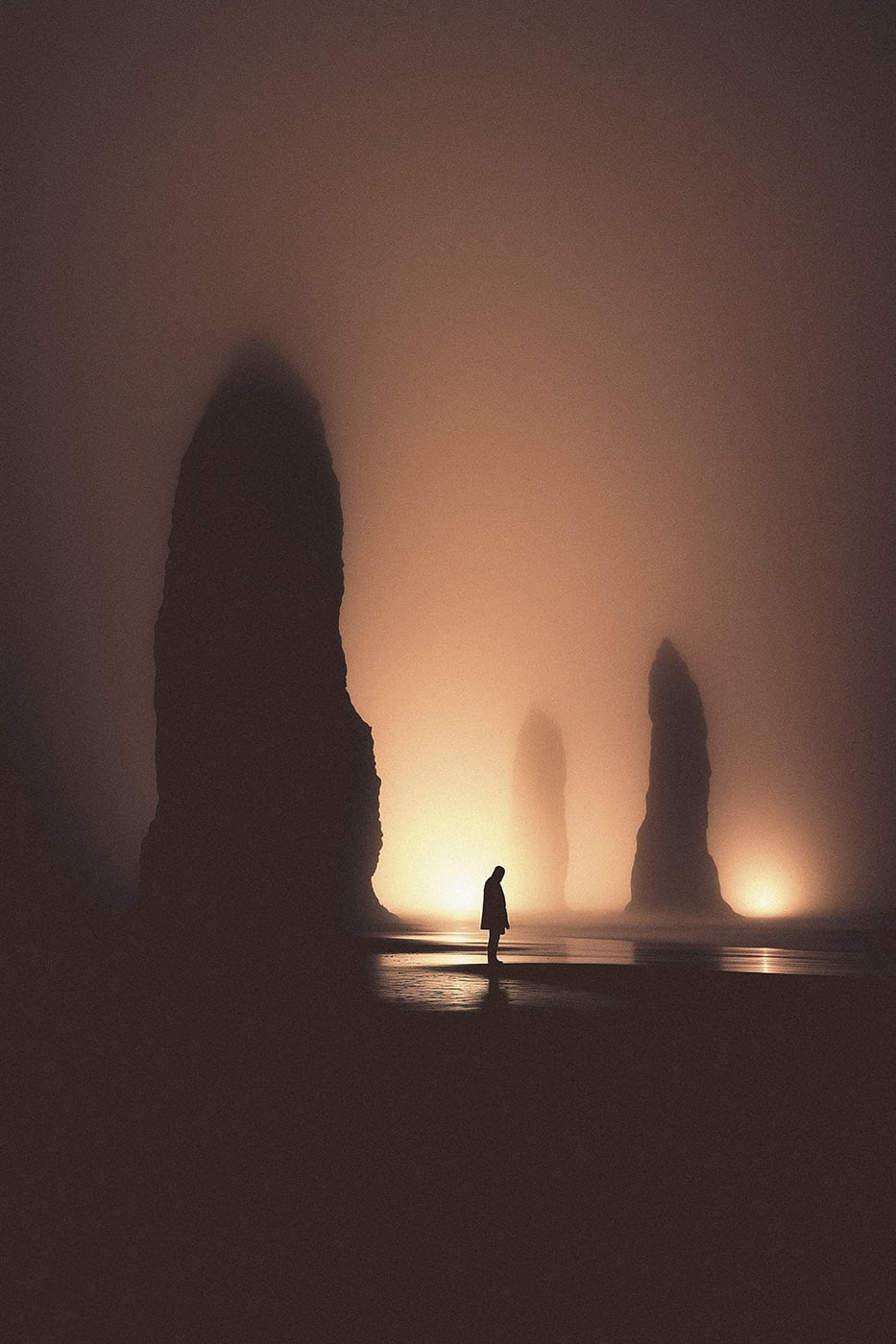 A mysterious hooded person in a surrealist beach landscape. A mysterious light breaks through the thick fog and shines on the monumental cliff structures at the shore. | Wall Art