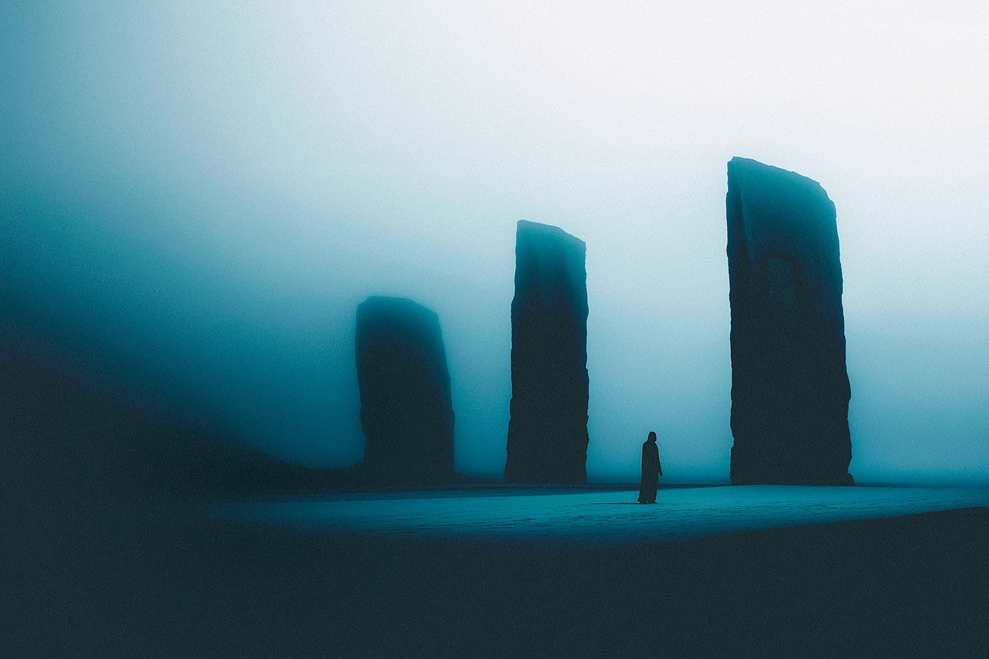 A mysterious hooded person in a vast, empty landscape, with huge rock formations covered in blue mist. A journey into the mind. | Wall Art